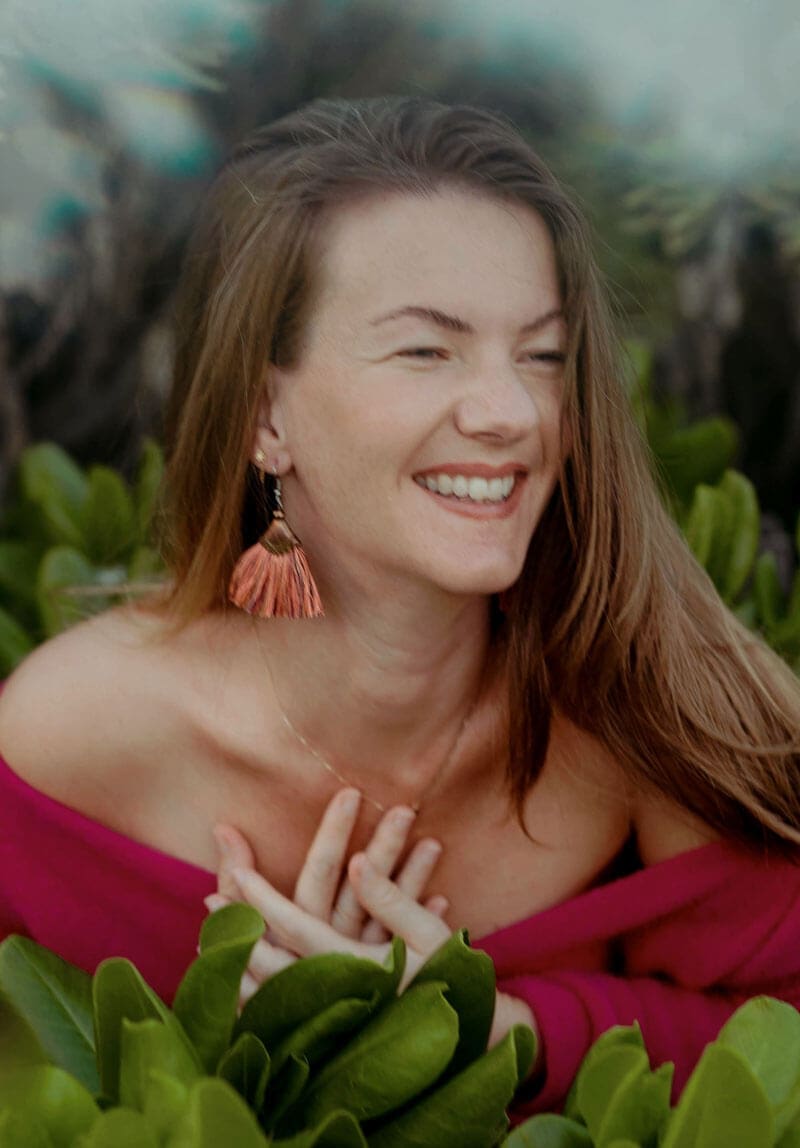 Eva smiling in a red dress surrounded by green leaves